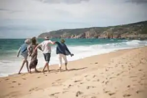 Family walking along the shoreline on a sunny day at Cornwall beach.