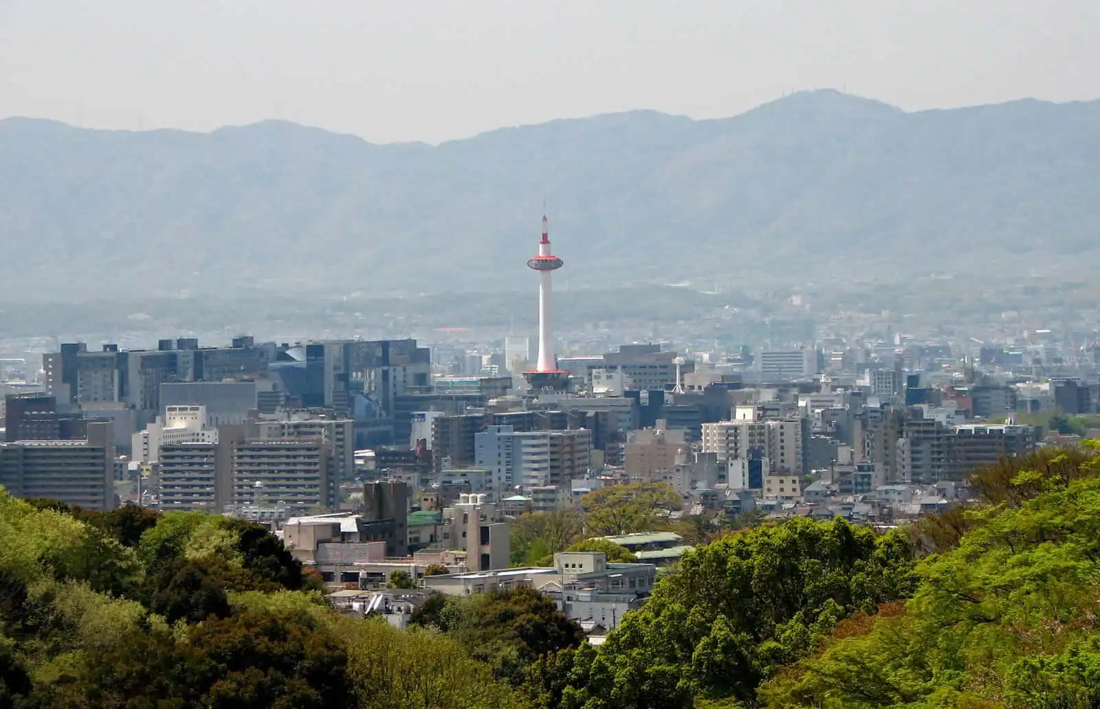 Kyoto skyline featuring Kyoto Tower with lush green foreground and distant mountains in the backgrou.