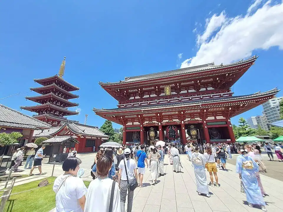 Japanese temple with visitors, pagoda, and clear blue sky.
