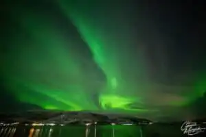 Aurora borealis dancing across the night sky above snow-covered mountains in Norway.